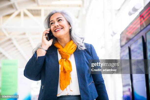 シニア ヒスパニック系女性空港でスマート フォンを使用して