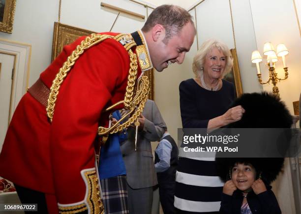 Camilla, Duchess of Cornwall helps Lara Mehmet, 9 to try on a guardsman's bearskin during an annual event to decorate the Clarence House Christmas...