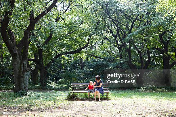 mother and baby sit on bench in forest. - mum sitting down with baby stockfoto's en -beelden
