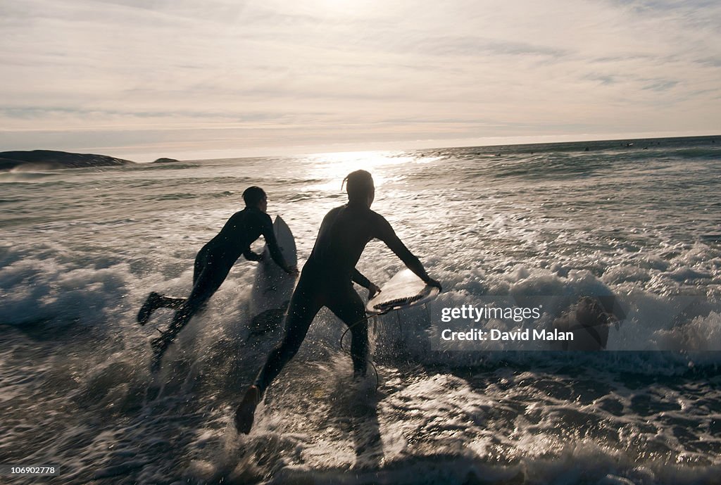 Two surfers leaping into the water at sunset.