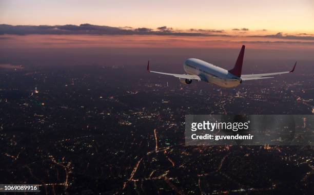 commercial airplane flying over big city at dusk - air travel stock pictures, royalty-free photos & images