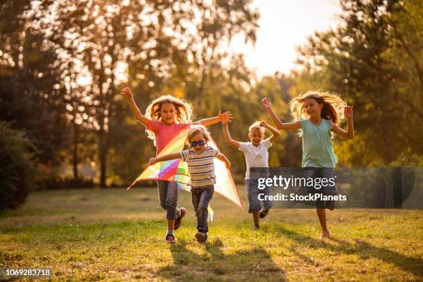 grupo de niños felices corriendo en el parque público - jugar fotografías e imágenes de stock