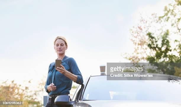 portrait of a mid adult businesswoman leaning against her car reading text messages - digital devices beside each other stockfoto's en -beelden