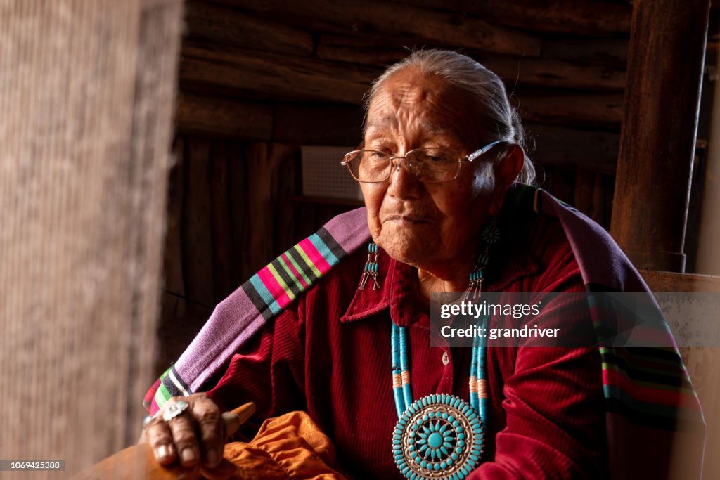 Elderly Native American Navajo Woman Weaving a Traditional Tribal Blanket on a loom inside a Hogan