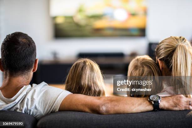 achteraanzicht van een ontspannen familie tv kijken op de sofa in de woonkamer. - family watching tv from behind stockfoto's en -beelden