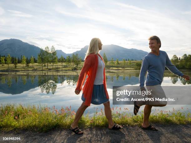 couple walk along lake edge, on path in mtns - woman side view walking stock pictures, royalty-free photos & images