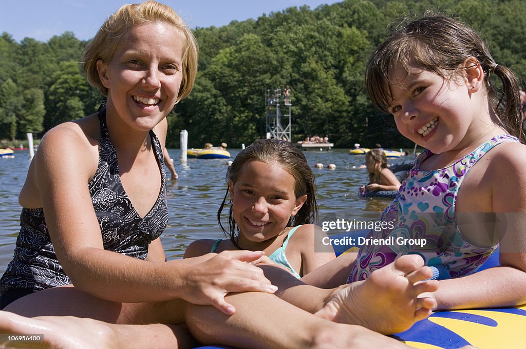 A Mom with kids floating on a raft in a lake.