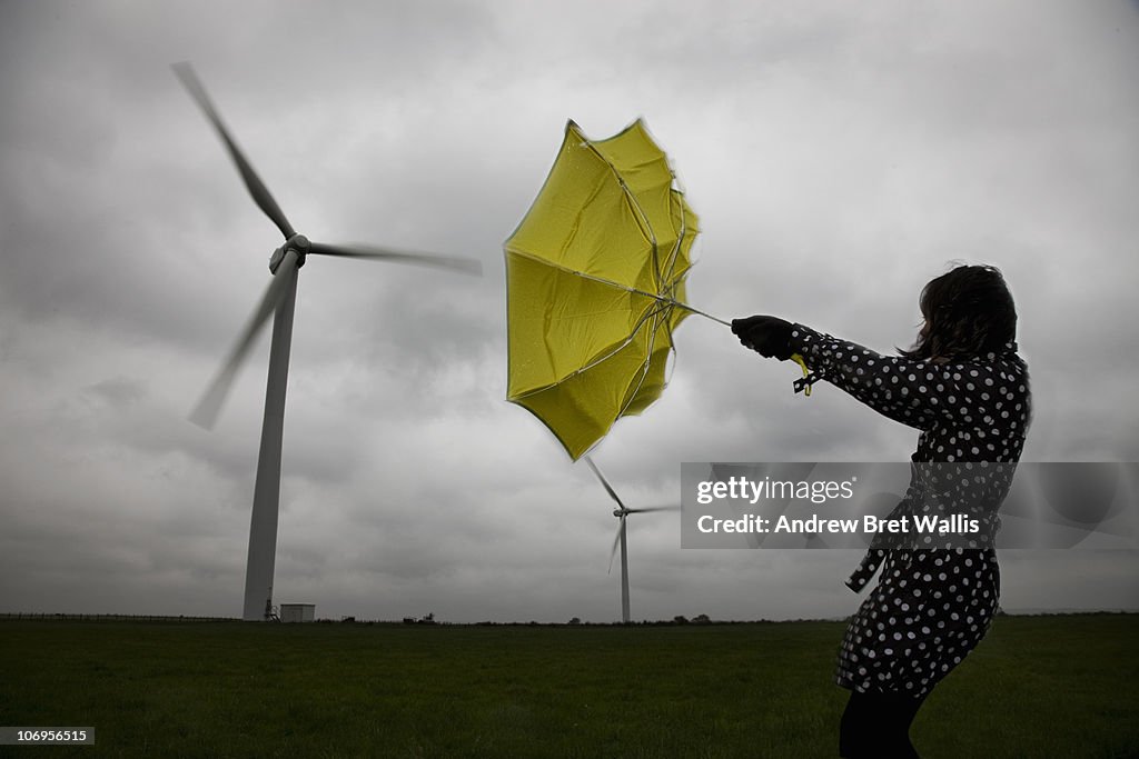 Woman holding umbrella beneath wind turbines