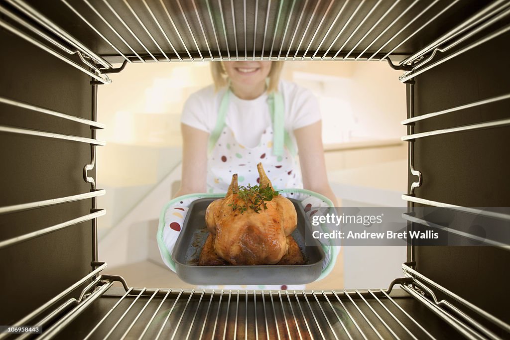 Woman taking freshly cooked chicken out of an oven