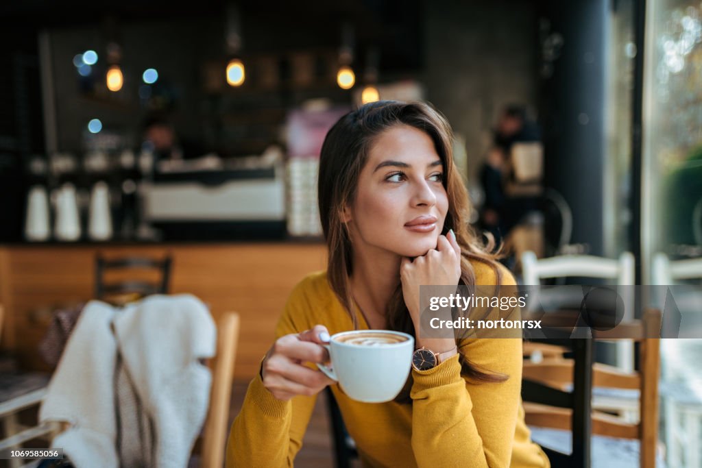 Stylish young woman drinking coffee at the cafe, looking away.