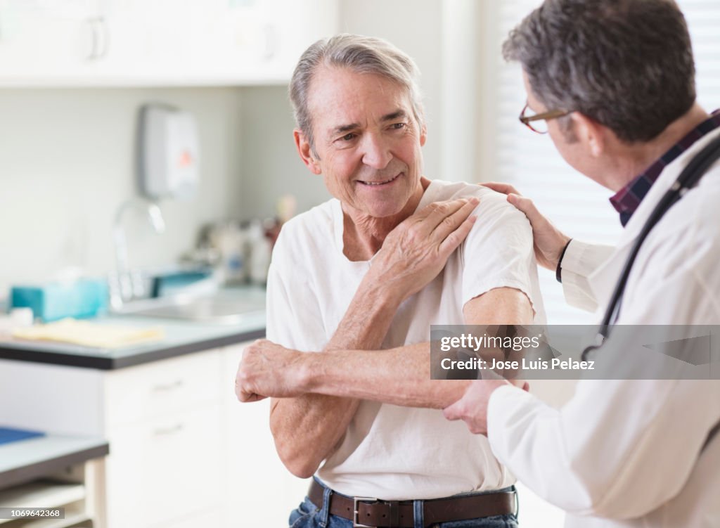 Senior patient explaining shoulder pain to doctor in clinic