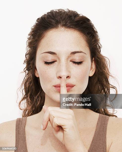 young woman with finger on lips, eyes closed - finger on lips stock-fotos und bilder