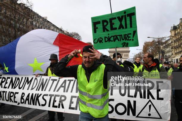 Demonstrator gestures in front of placards, one of which says 'Frexit car dictature!' during the demonstration of the yellow vests at the Arc de...