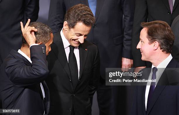 President Barack Obama makes a 'rabbit ears' gesture as he stands with French President Nicolas Sarkozy and British Prime Minister David Cameron...