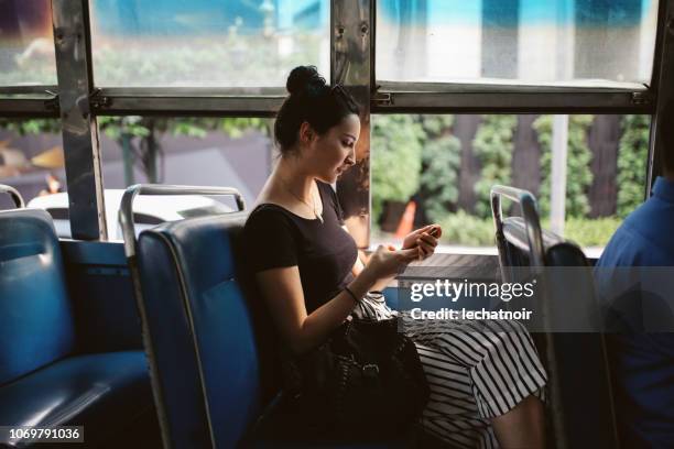 mensajes de texto de mujer joven en un teléfono móvil en un autobús público en bangkok, tailandia - bus interior fotografías e imágenes de stock