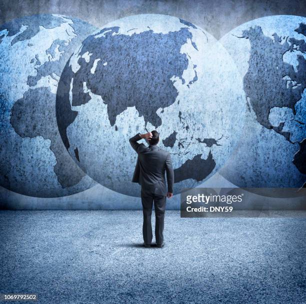 geschäftsmann steht und schaut sie an drei ineinandergreifenden globes an wand - international politics stock-fotos und bilder