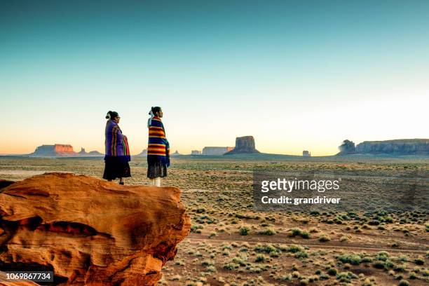 twee traditionele navajo indiaanse zusters in monument valley tribal park op een rotsachtige butte genieten van een zonsopgang of zonsondergang - culturen stockfoto's en -beelden