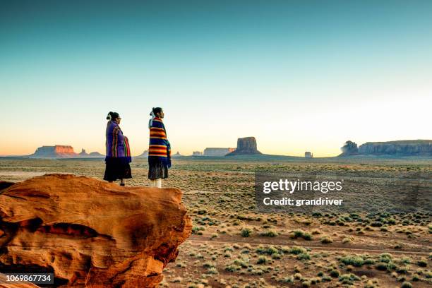 two traditional navajo native american sisters in monument valley tribal park on a rocky butte enjoying a sunrise or sunset - aboriginal family stock pictures, royalty-free photos & images