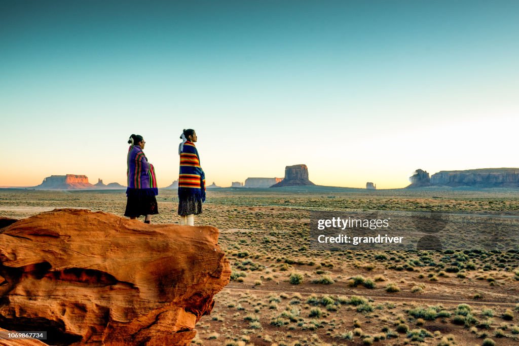 Duas tradicionais Navajo nativo americanas irmãs em Monument Valley Tribal Park em uma colina rochosa apreciar um nascer ou pôr do sol