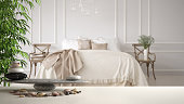 White table shelf with pebble balance and bamboo plant over vintage classic bedroom with soft bed full of pillows and blankets, zen concept interior design