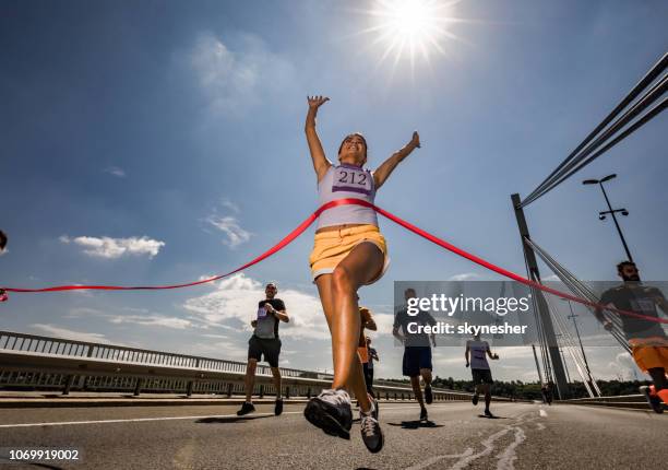 abajo vista de exitoso maratonista cruzando la línea de meta. - carrera de carretera fotografías e imágenes de stock