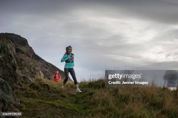 a woman out running down a mountain trail. - edinburgh scotland autumn stock pictures, royalty-free photos & images