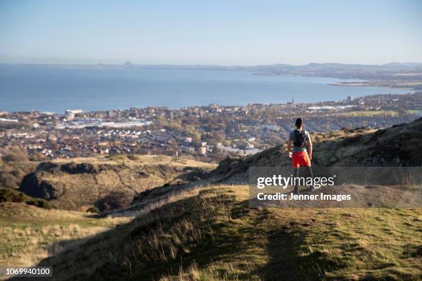 a male trail runner looking at the view of edinburgh from arthur's seat. - midlothian scotland stock pictures, royalty-free photos & images