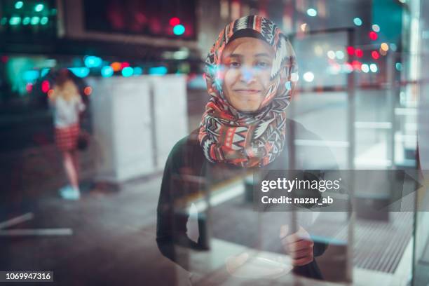 junge muslimische frau an bushaltestelle bus warten. - auckland city people stock-fotos und bilder