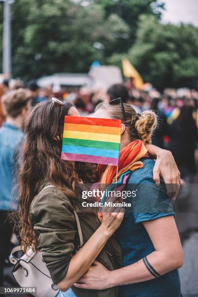 female couple kissing behind a rainbow flag - pride march stock pictures, royalty-free photos & images
