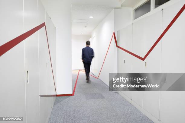 a red graphic chart on the wall and floor of the corridor, and a man walking - color boost stock-fotos und bilder