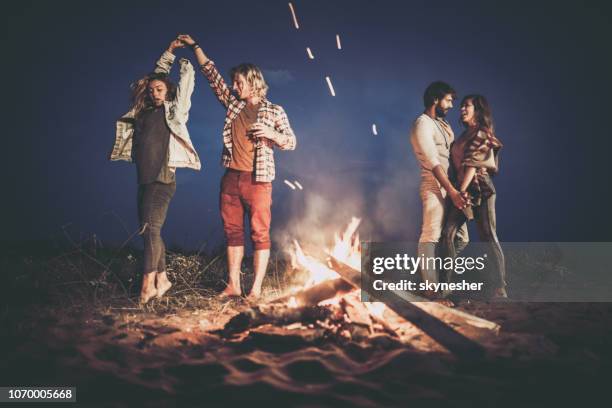 two happy couples dancing on a night party by the campfire. - bonfire beach stock pictures, royalty-free photos & images