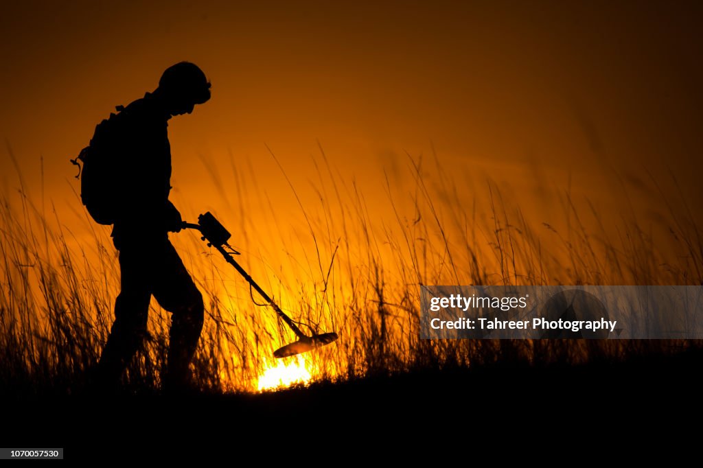 Silhouette of a man carrying an underground metal detector and looking for mines