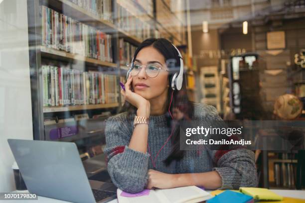 junge frau, die arbeitet auf ihrem laptop in der bibliothek - headphones woman stock-fotos und bilder