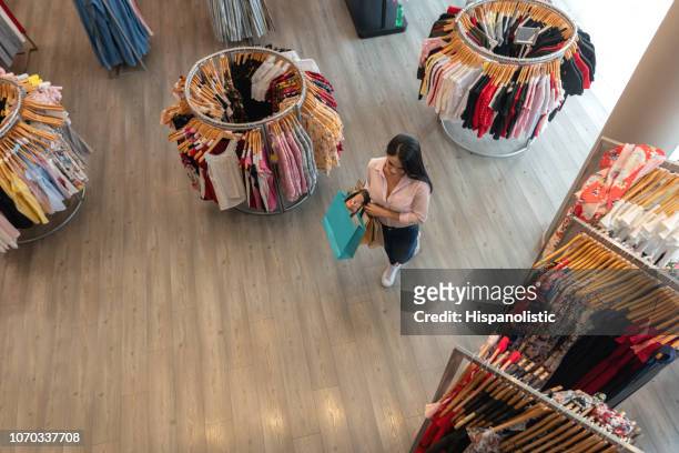 latin american woman walking at a clothing store while holding shopping bags - department store stock pictures, royalty-free photos & images