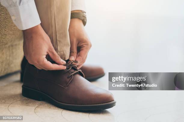 businessman with leather shoes tying shoe laces - zapatos marrones fotografías e imágenes de stock