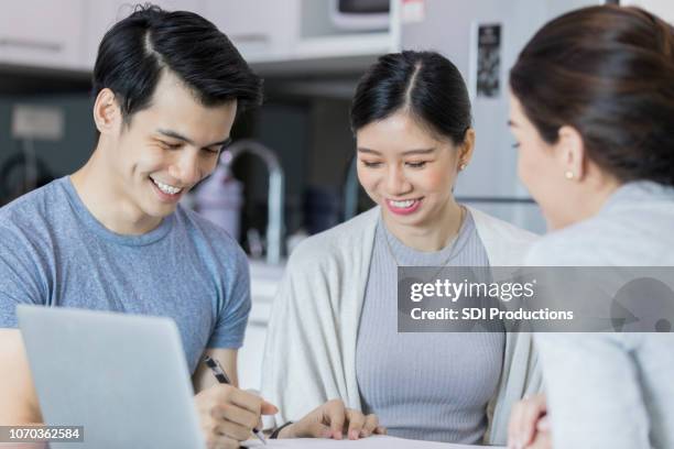 a young couple smile as the man signs a paper and the financial counselor watches - malaysia house stock pictures, royalty-free photos & images