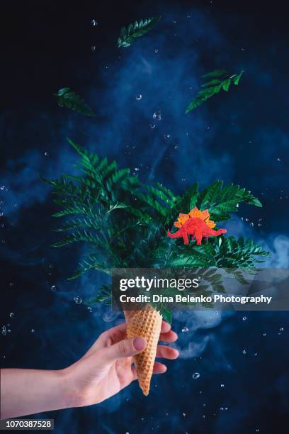 fern bouquet with a dinosaur in an ice cream cone with water droplets. weird ice cream on a dark background - fossil hunting stock pictures, royalty-free photos & images