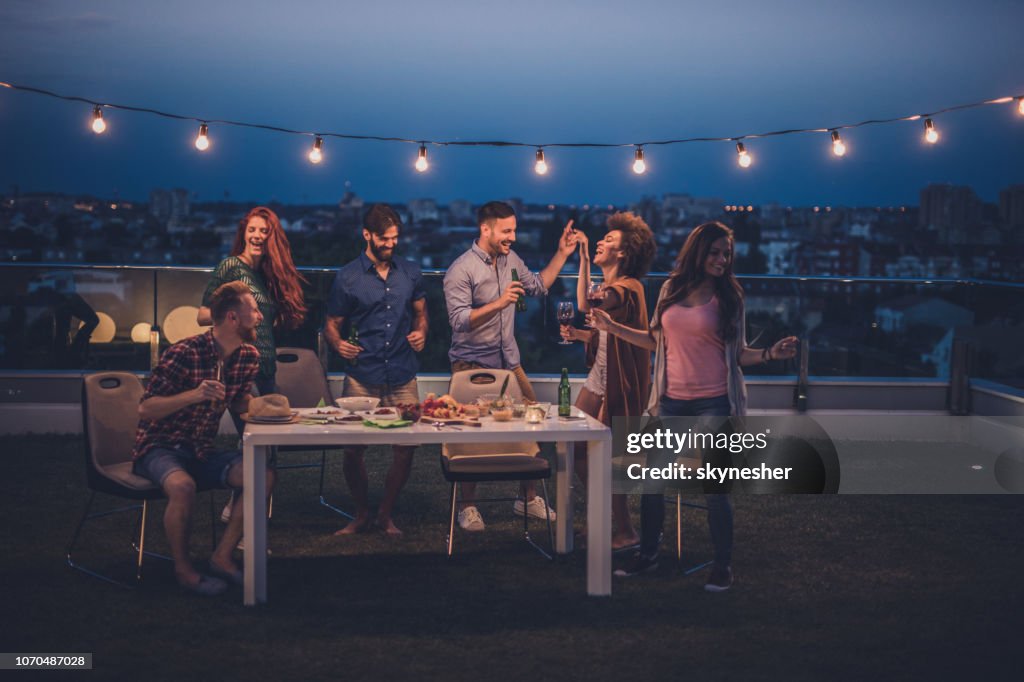 Young happy people having fun while dancing on a night party at penthouse balcony.