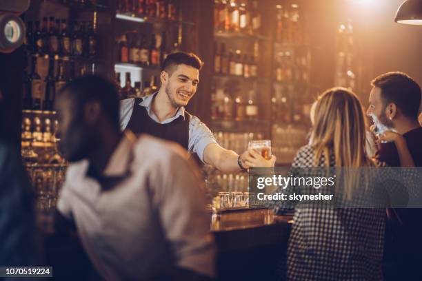young happy bartender serving beer to his customers in a bar. - bartender stock pictures, royalty-free photos & images