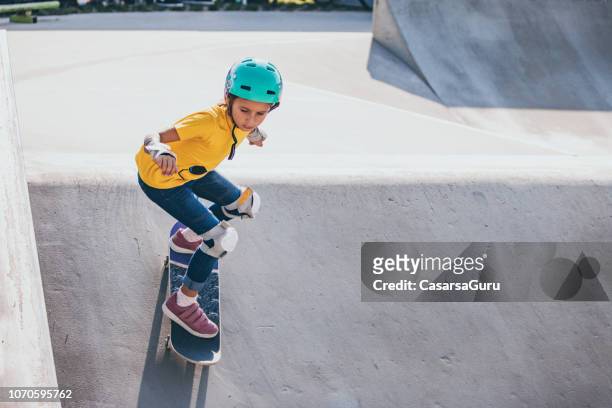 young skateboarding girl dropping from a bank in skatepark - skating stock pictures, royalty-free photos & images