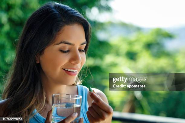 jonge spaanse vrouw klaar om te nemen van een pil met een glas water in de hand - sun flare on glass stockfoto's en -beelden