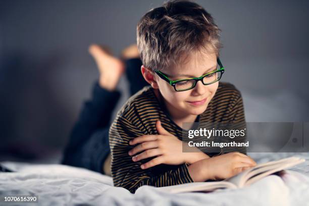 little boy reading a book on bed - reading glasses stock pictures, royalty-free photos & images