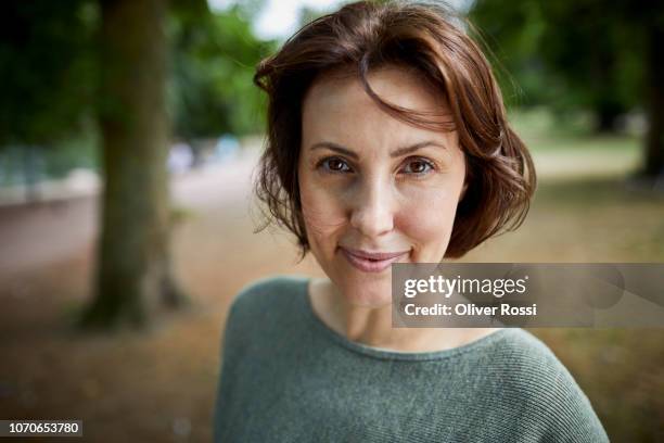 portrait of smiling brunette woman in a park - cabello castaño fotografías e imágenes de stock