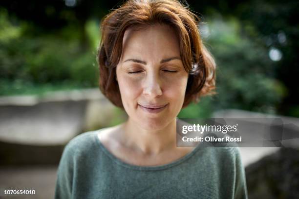 portrait of smiling brunette woman with closed eyes in a park - brunette woman foto e immagini stock