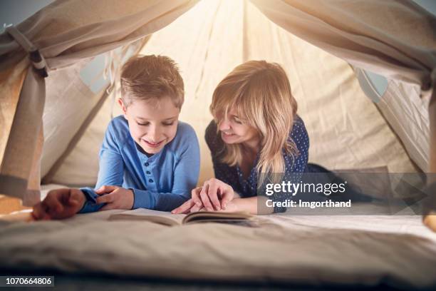 mother and son reading a book in teepee tent - teepee stock pictures, royalty-free photos & images