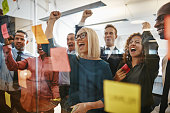 Businesspeople cheering while brainstorming with sticky notes in an office