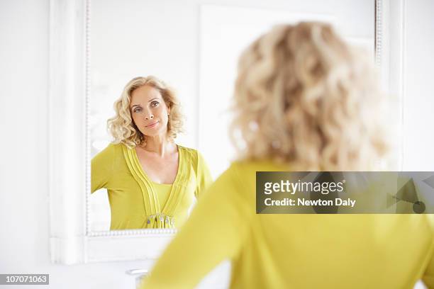 mature woman looking in mirror - woman mirror stockfoto's en -beelden