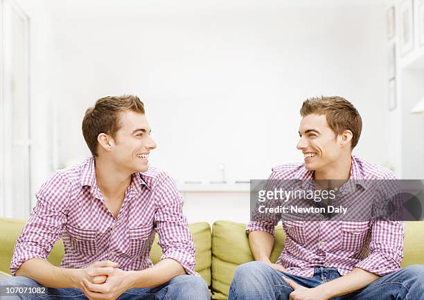 twins sitting on sofa, smiling - twin stock pictures, royalty-free photos & images