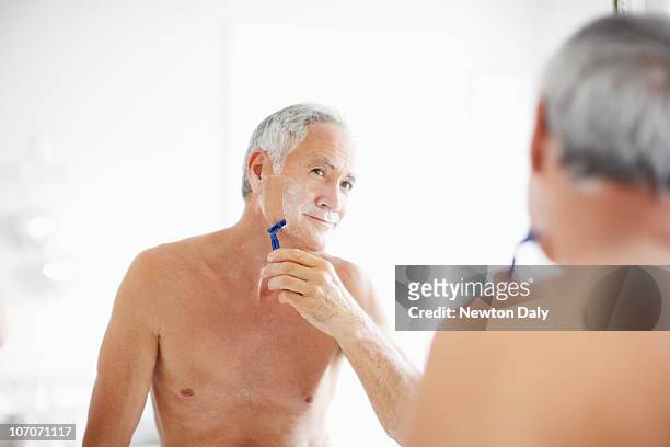 senior man shaving in mirror - scheermes stockfoto's en -beelden