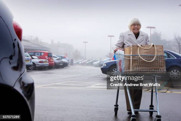 senior female pushing a supermarket trolley - shopping trolley photos et images de collection